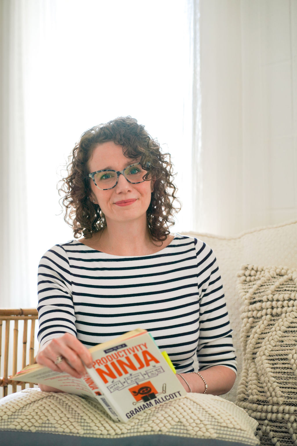 Jessie on a sofa in a striped top, holding a book and smiling